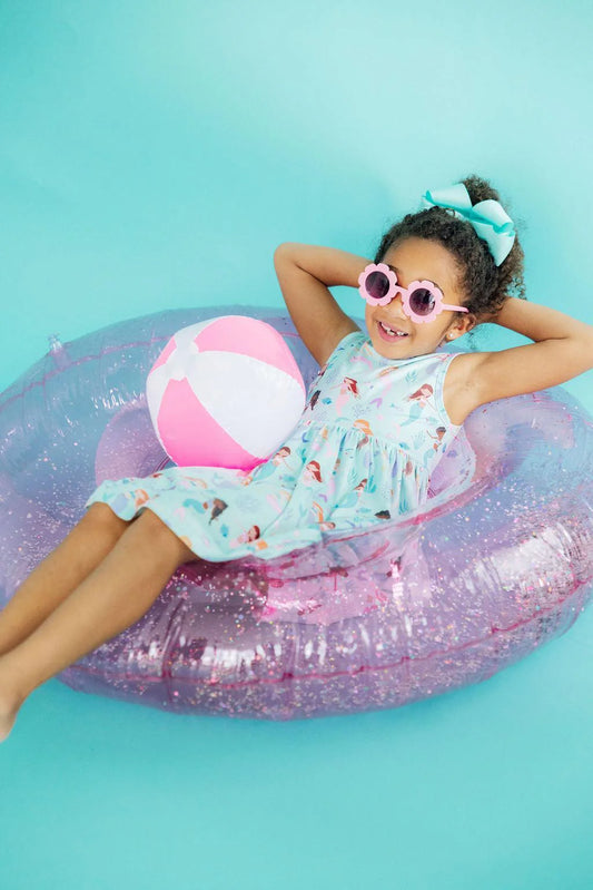 girl wearing blue sleeveless twirl dress with colorful mermaid, shell, and sea creature pattern while sitting in a pool float
